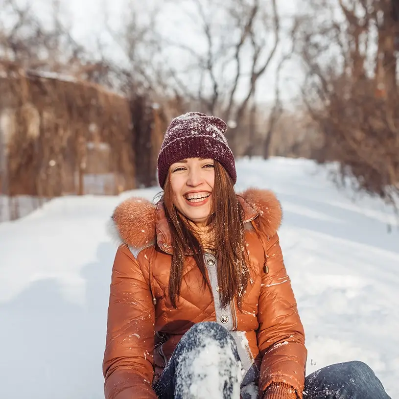Kobieta siedząca na śniegu i śmiejąca się, nie mająca objawów przeziębienia lub alergii.