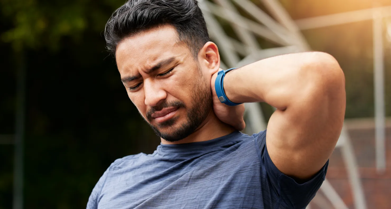 A man suffering with a neck ache. He's touching his neck with his hand and seems to have discomfort.