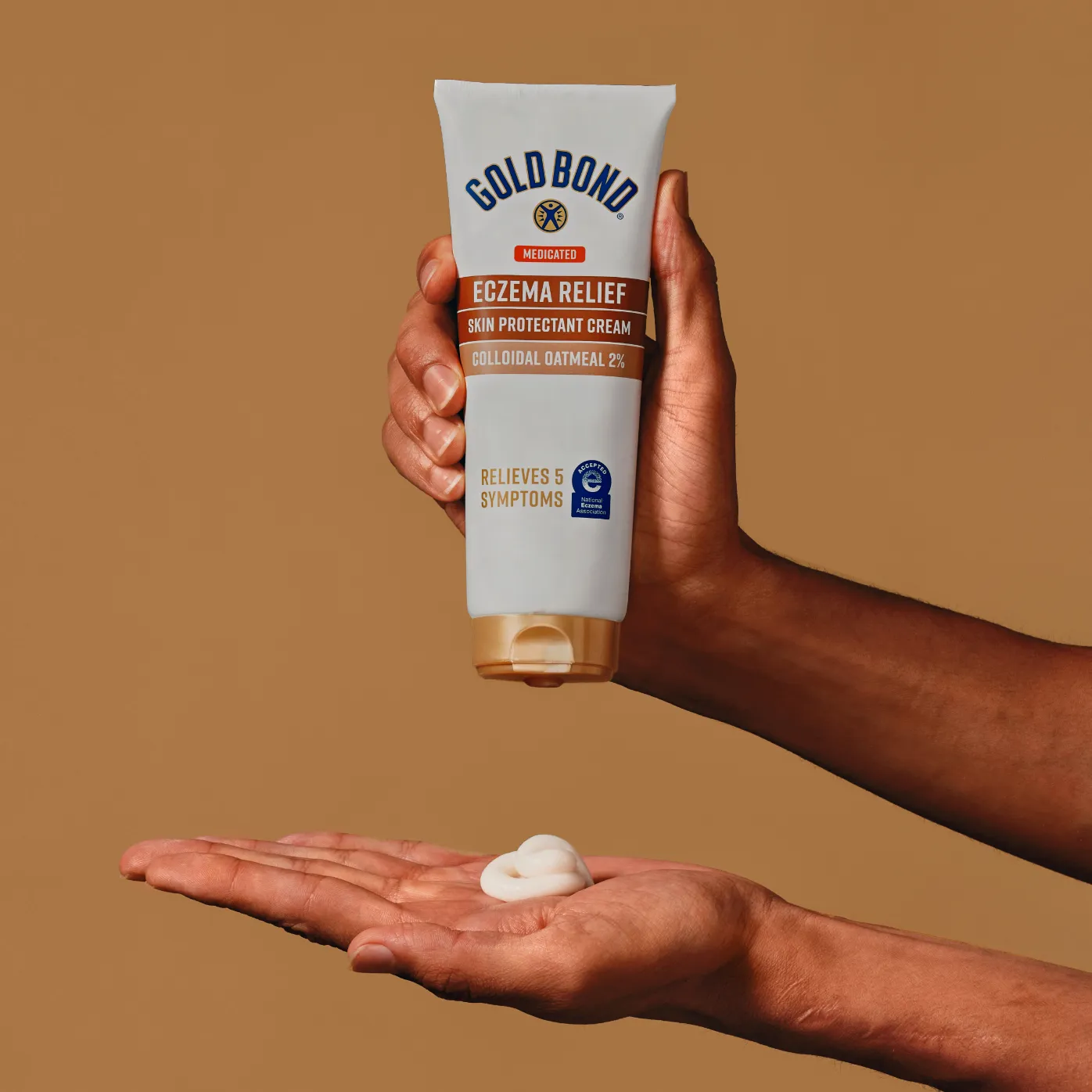 A hand squeezing a container of Gold Bond Eczema Relief cream, with the white cream visible on the other hand.