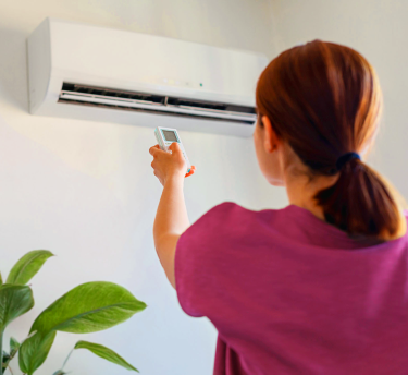 Woman adjusting air conditioning with a remote, suggesting temperature changes as an allergy trigger
