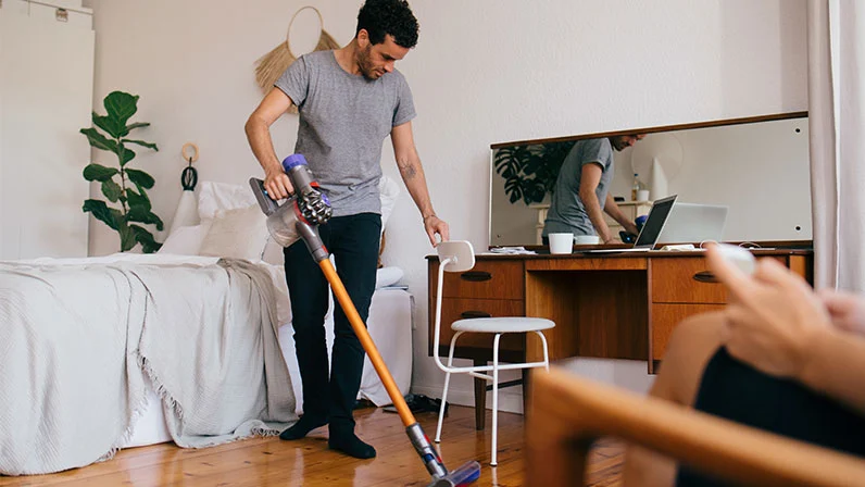 Mężczyzna odkurzający sypialnię w środku dnia, aby pozbyć się przyczyn powodujących alergię wewnątrz pomieszczeń.