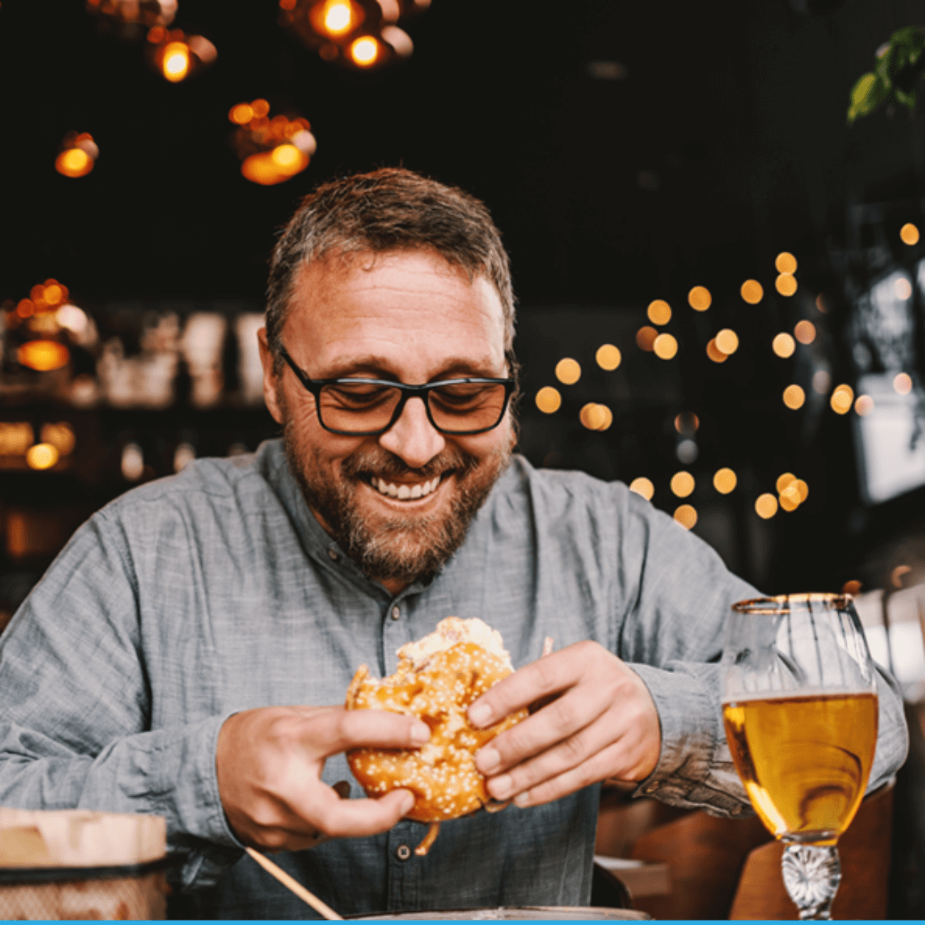 A man sitting in a restaurant happily enjoying a beer and a sandwich.