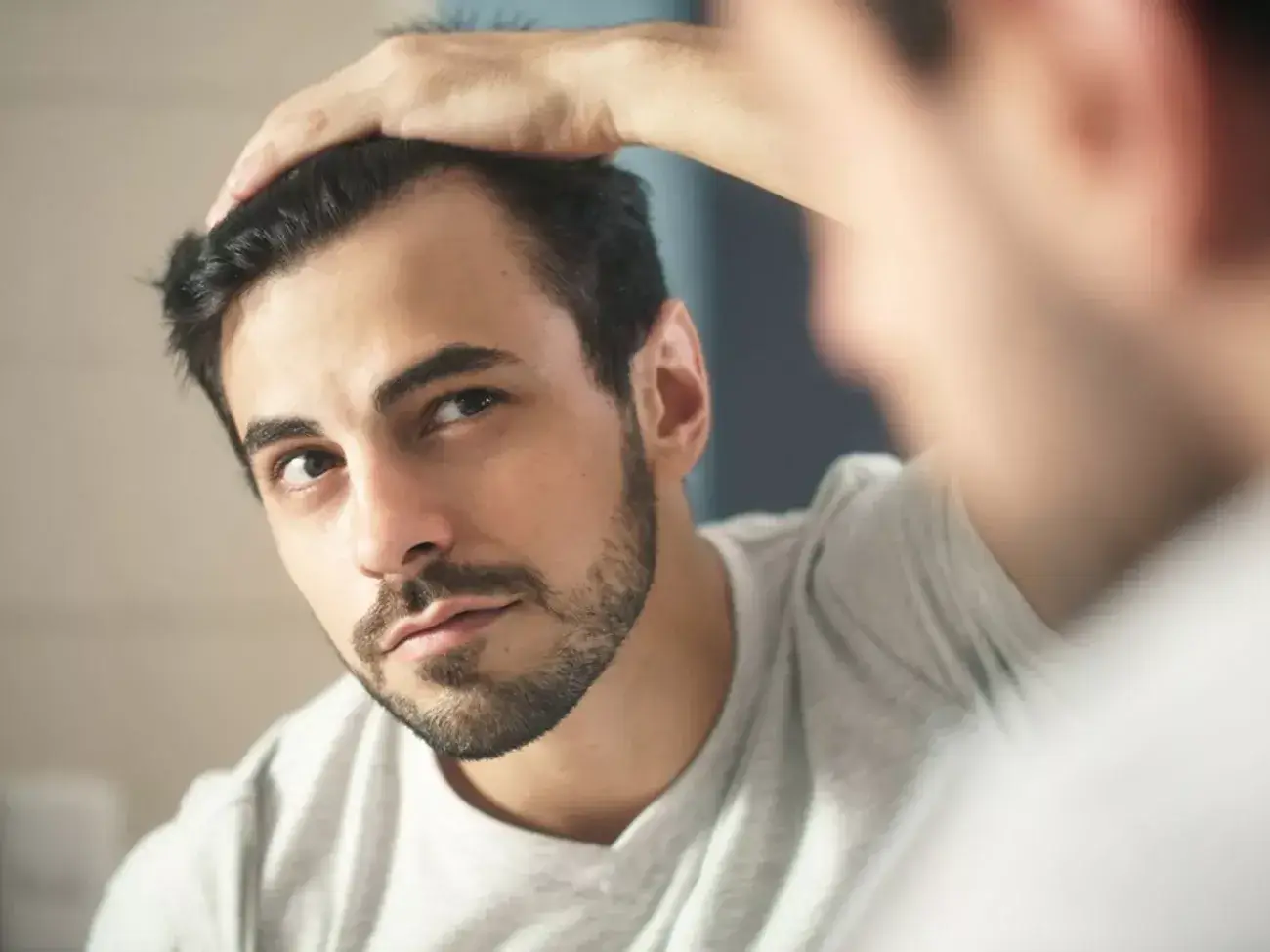 A man looking at himself in the mirror while pushing his hair back.