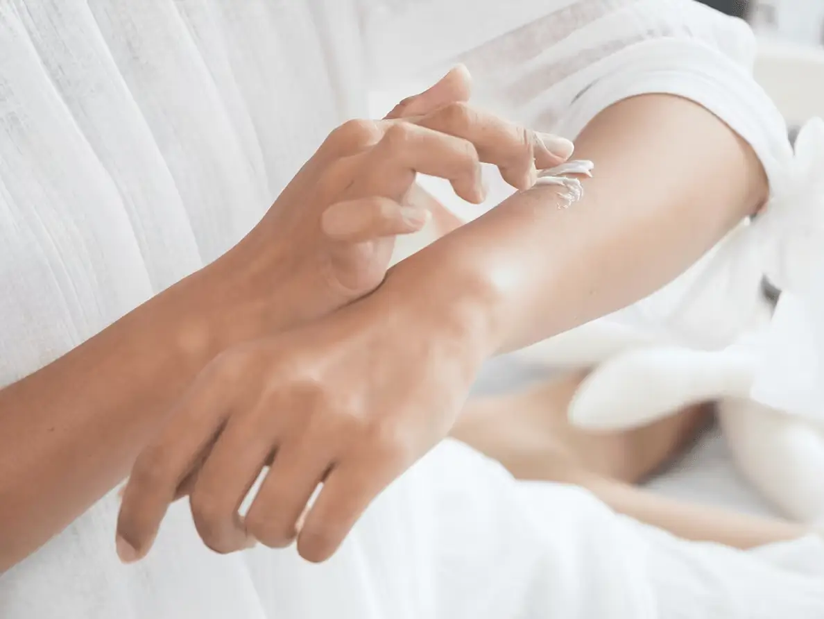 A woman rubs cream into her hands.