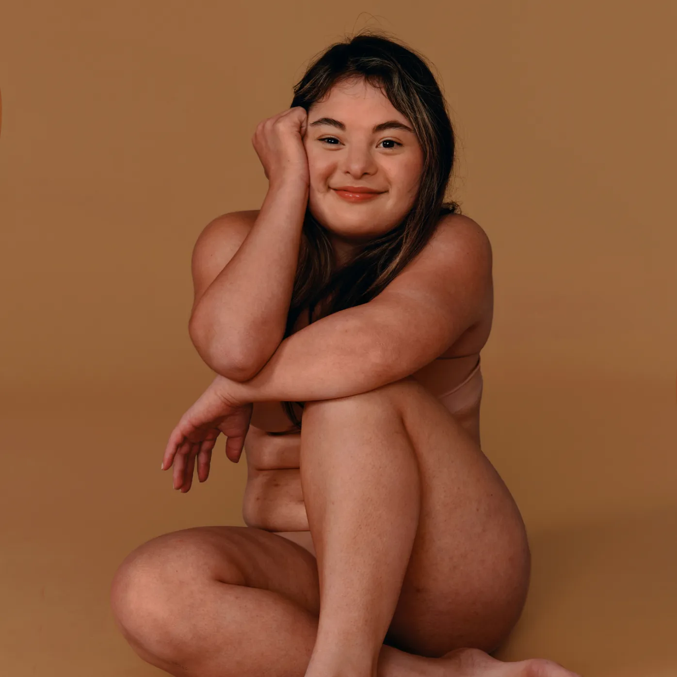 A woman with a warm smile, posing for the camera on a beige background.
