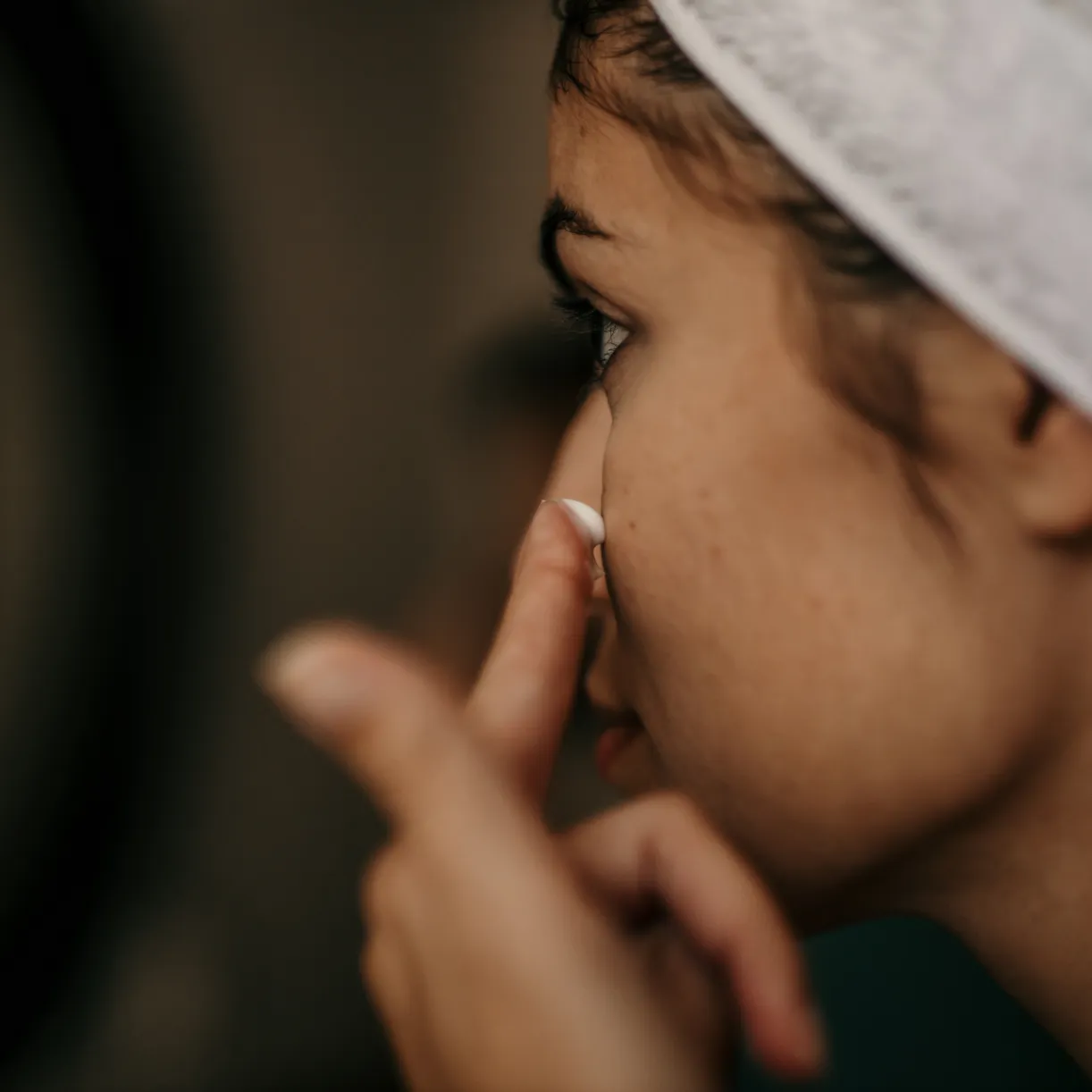 An image of a womans face with symptoms of dry skin and applying a bit of cream.
