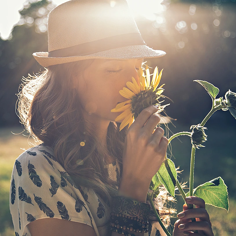 A woman stands in a field and smells a sunflower.