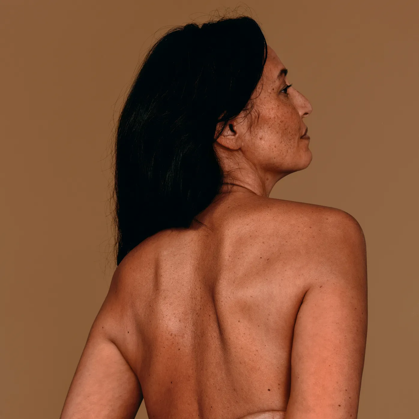 A woman with long dark hair looking to the side, revealing the graceful curve of her back