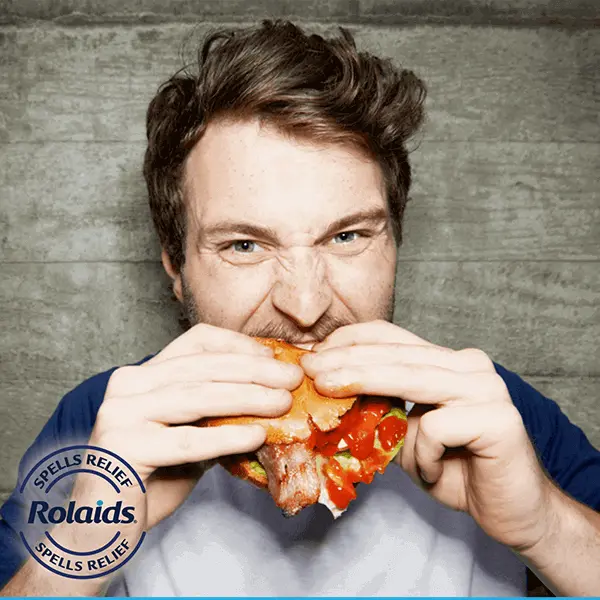 A man ferociously eating a bacon burger.
